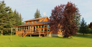 A wooden lodge with a deck and a satellite dish, surrounded by trees and a clear sky. - Bear Den - Unique Alaskan log home in trees & wildflowers on 14-acre homestead. (Anchor Point)