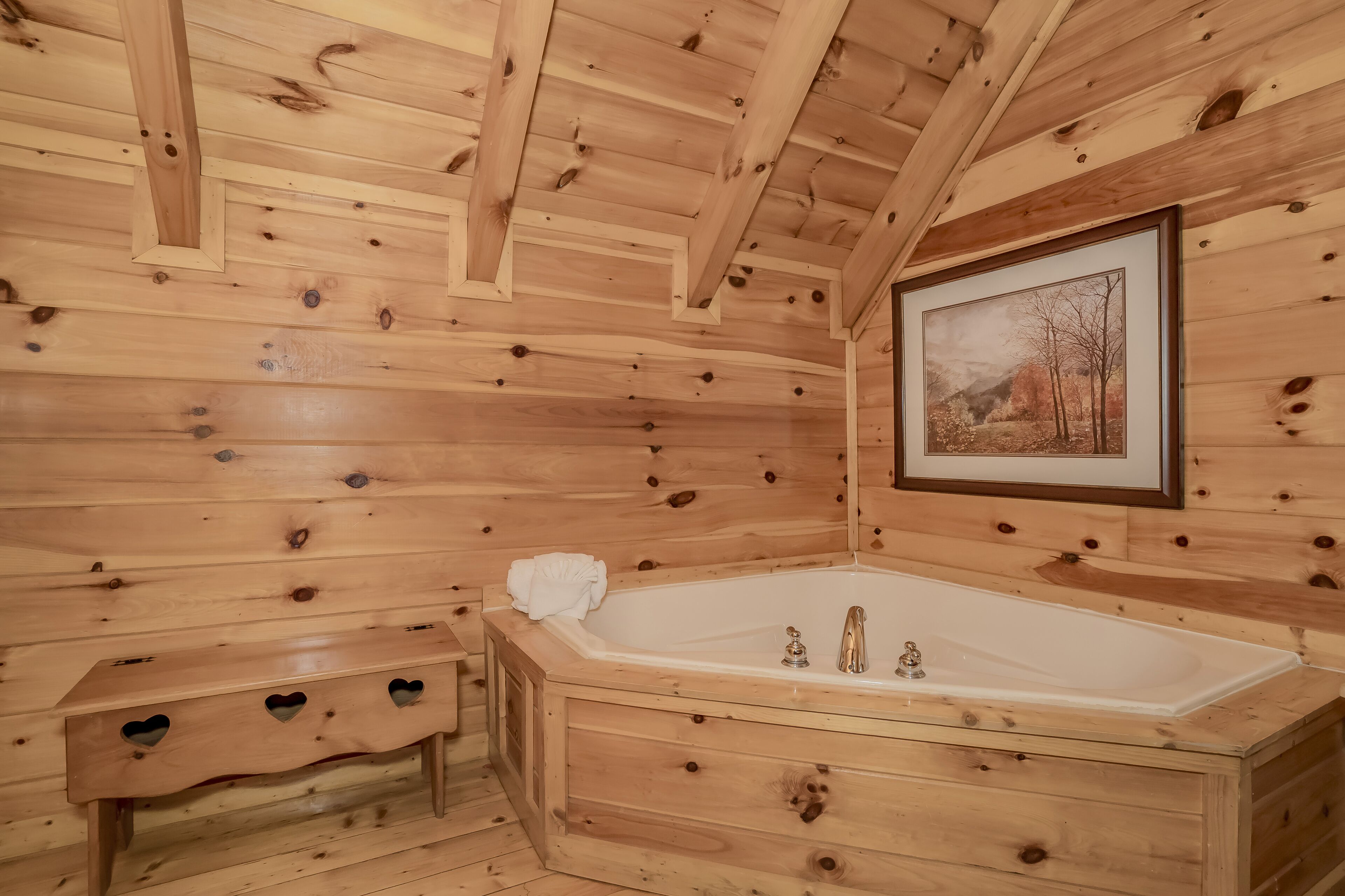 A wooden cabin bathroom with a bathtub, wooden bench, and a framed picture on the wall.