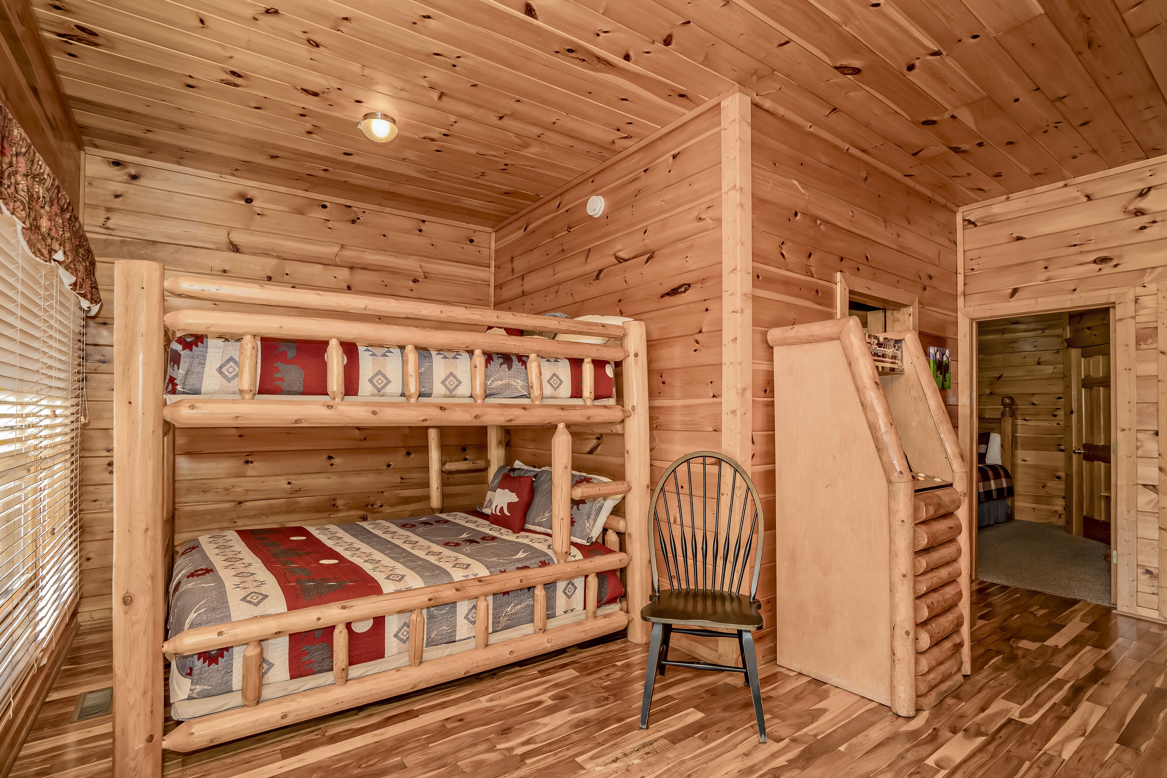 Ein Blockhauszimmer mit einem Etagenbett, einem Sessel und einer Treppe, die in einen anderen Raum führt.
