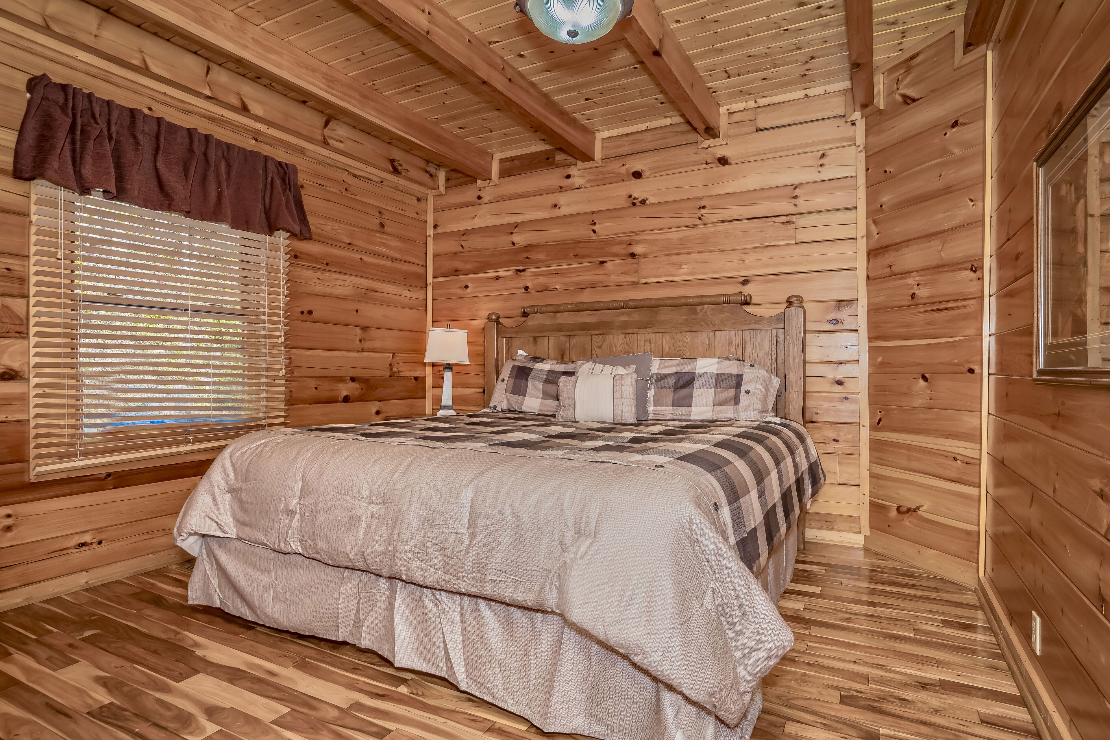 Un dormitorio de cabaña de madera con una cama, una ventana con persianas, una lámpara y una luz en el techo.