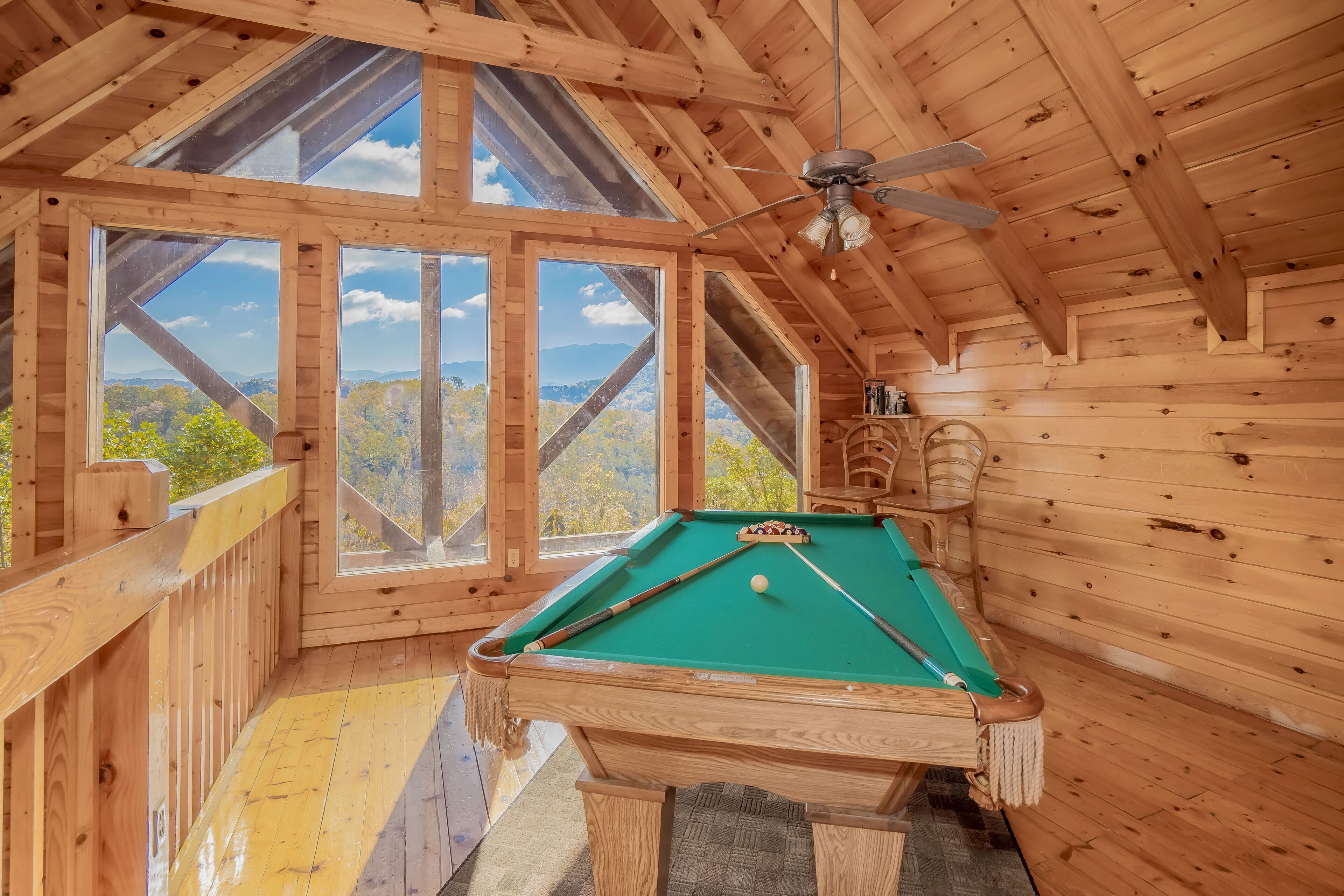 Une pièce en bois avec une table de billard, de grandes fenêtres et un ventilateur de plafond.