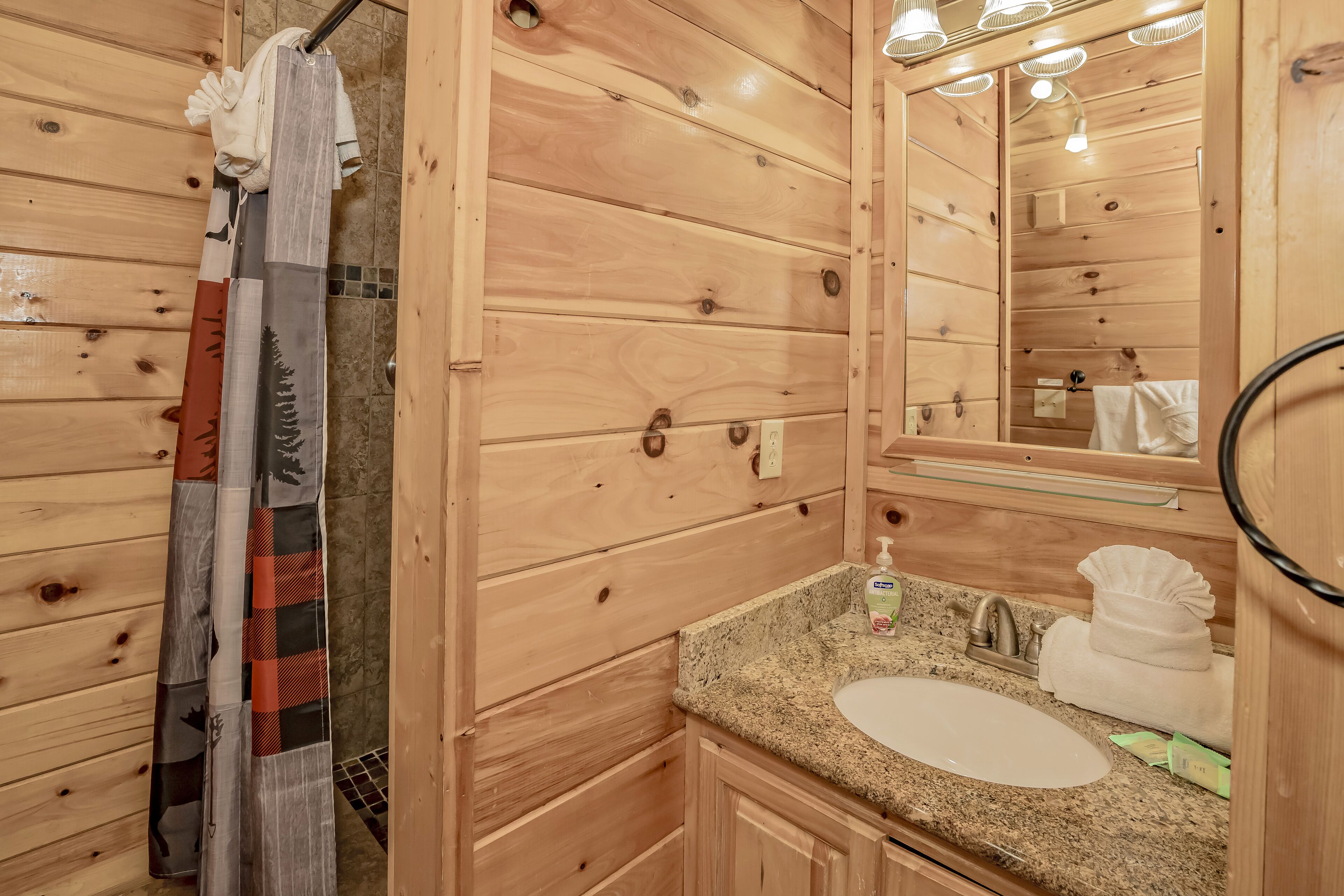 A wooden cabin bathroom with a granite sink, a mirror, and a shower curtain.