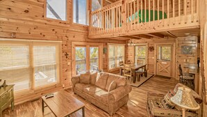 A spacious cabin with a loft bedroom, a cozy living area with a sofa, and a dining area. - 5 miles to Gatlinburg, Hot Tub, Views, 4 BEDROMS: JEEP INVASION, ROD RUN, SPARKS (Pigeon Forge)