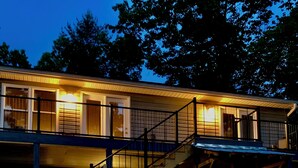 Un bâtiment à deux étages, avec une façade en bois, un escalier menant à l’étage supérieur et un espace extérieur aménagé avec des tables et des chaises.