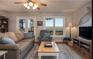 Relax in this inviting living room with a sofa, armchair, and large windows offering scenic mountain views.
