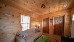 Interior de una cabaña de madera con un sofá, una mesa verde y un cartel que indica senderos para caminatas.