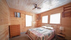 Un dormitorio de cabaña de madera con cama, cómoda y ventilador de techo.