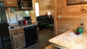Cocina compacta con lavavajillas, microondas y cafetera. Hay una mesa de madera con sandía y manzanas.