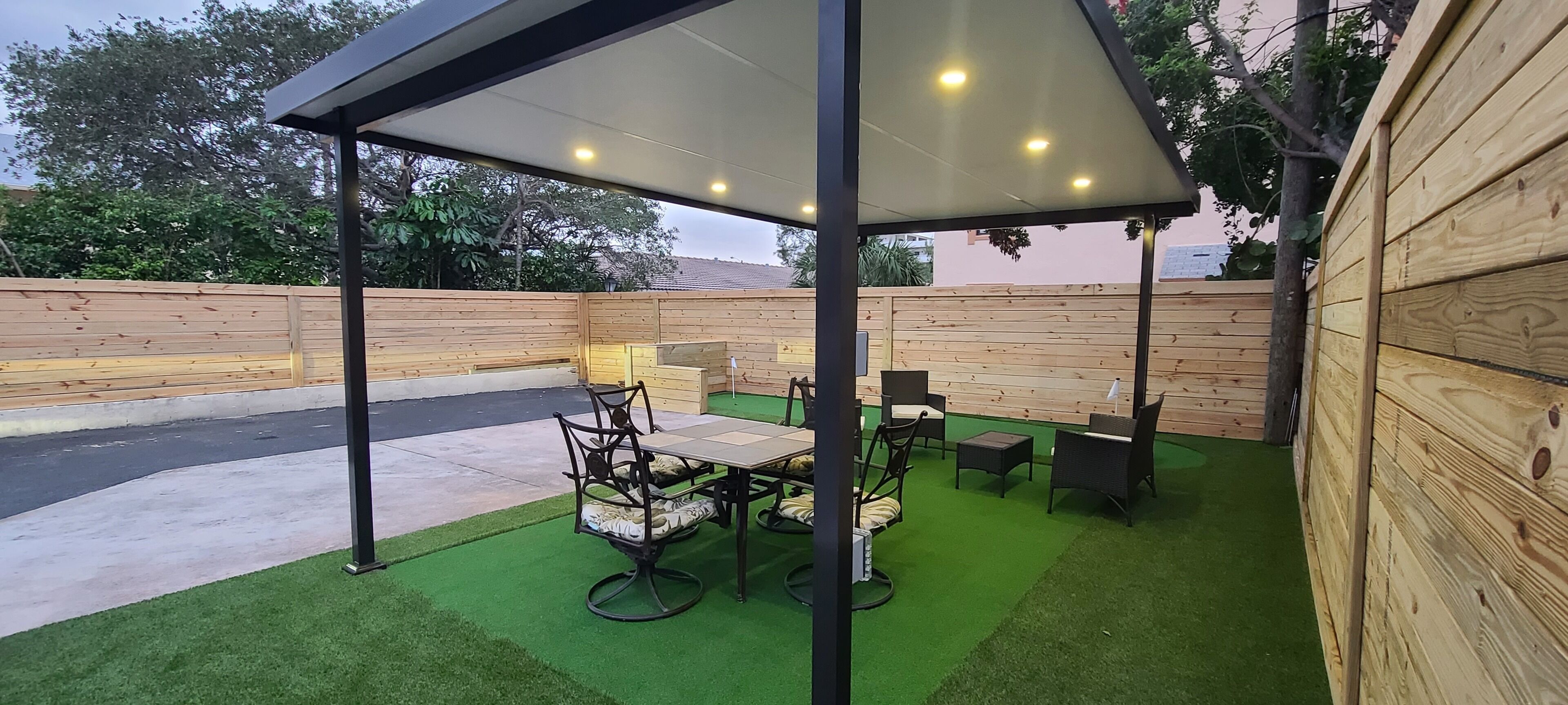 Un patio al aire libre con zona de estar techada, césped artificial y paredes de madera.