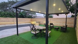An outdoor patio with a covered seating area, artificial grass, and wooden walls.
