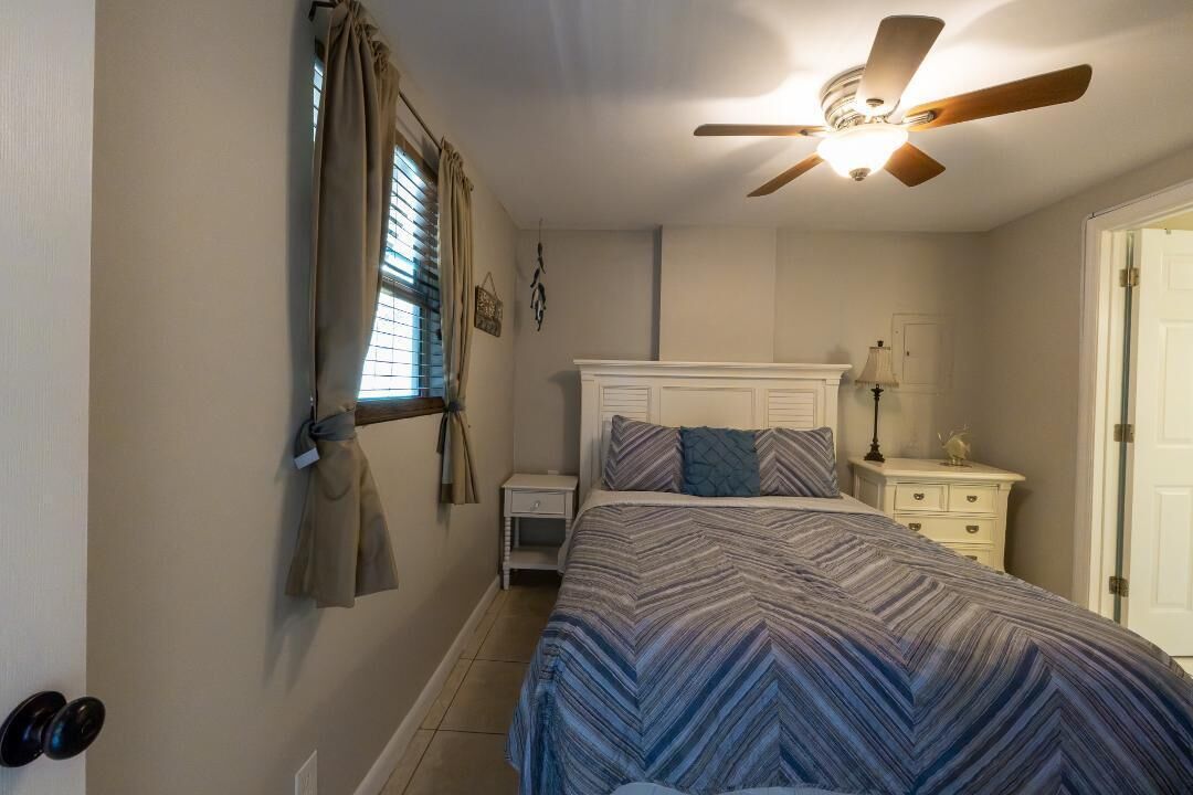 A bedroom with a bed, a ceiling fan, a nightstand, a lamp, and a door.