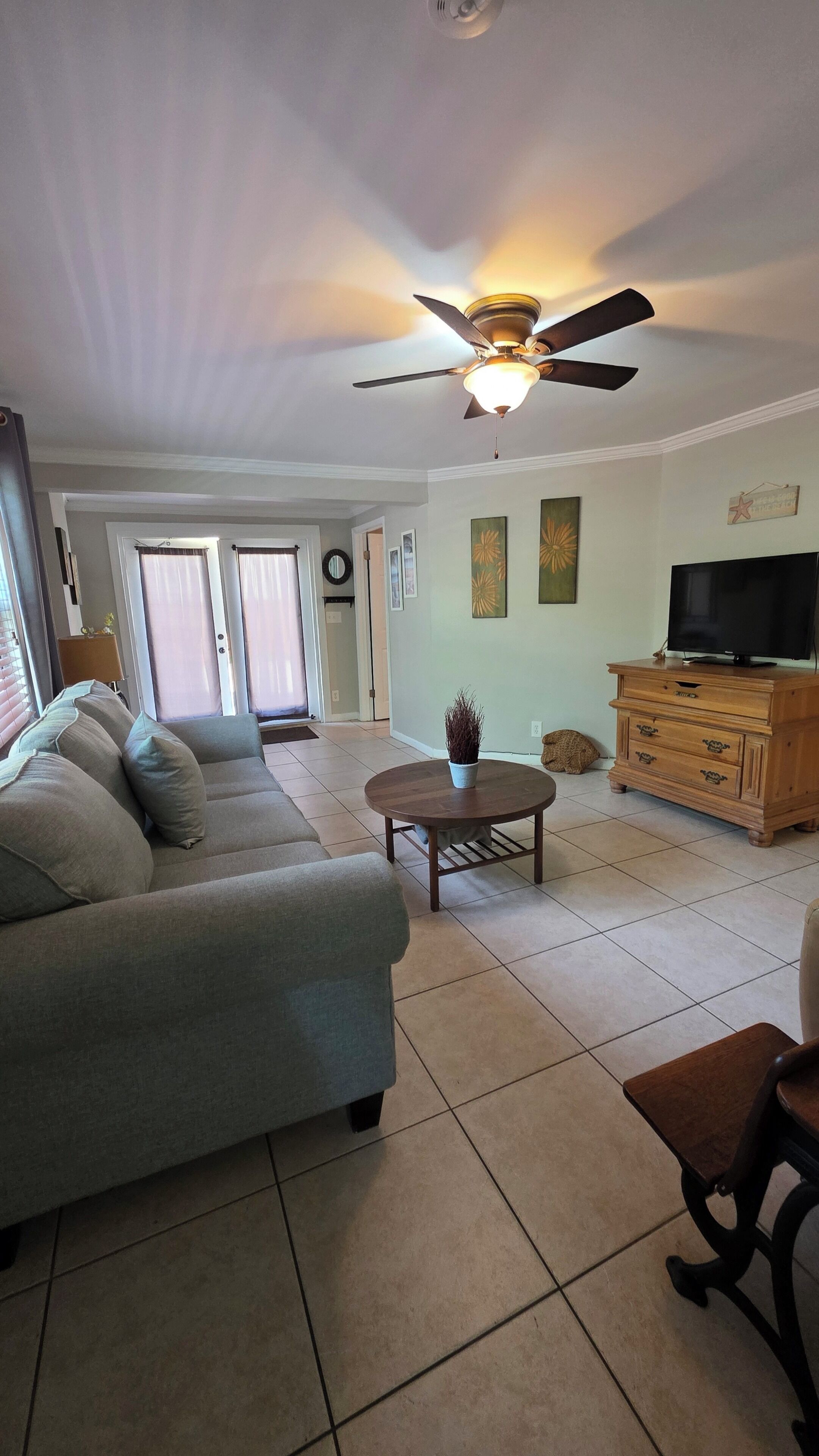 A living room with a sofa, a coffee table, a TV stand, and a ceiling fan.