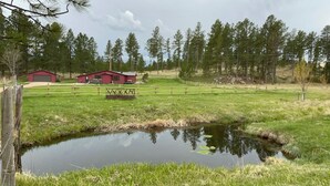 Paisaje rural con un estanque, un granero rojo y un área cercada.