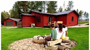 Una cabaña de madera roja con un hogar de piedra al frente.