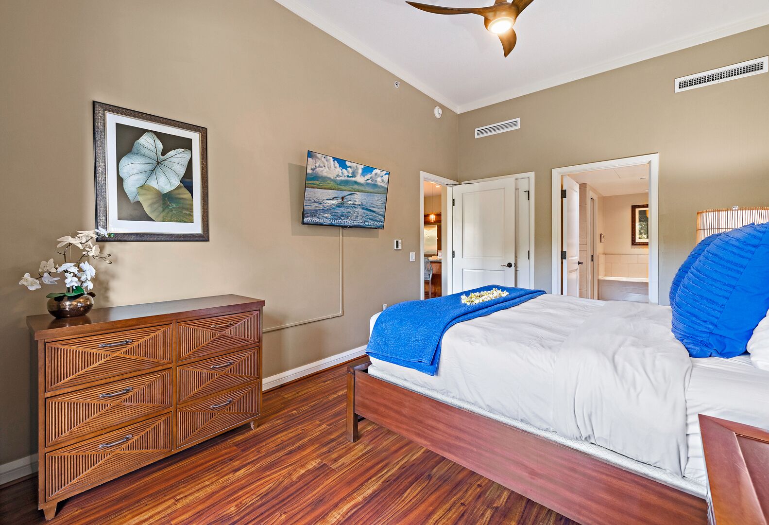 A bedroom with a bed, wooden dresser, and a ceiling fan.
