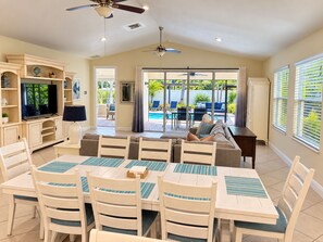 A spacious living room with a television, seating area, and a view of a pool.