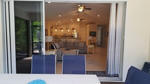 A dining area with a table and chairs, a kitchen in the background, and a sliding glass door leading to a balcony. - Naples Best Value Luxury 4 Bedroom Heated Pool Spa Bikes Spacious Backyard (Naples)
