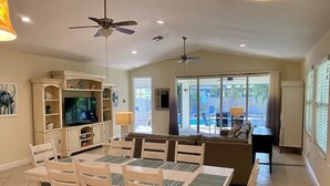 A dining area with a table and chairs, a television, and a sofa in the background. - Naples Best Value Luxury 4 Bedroom Heated Pool Spa Bikes Spacious Backyard (Naples)