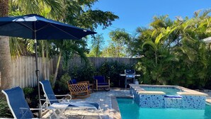 A backyard with a swimming pool, lounge chairs, a barbecue grill, and a wooden fence. - Naples Best Value Luxury 4 Bedroom Heated Pool Spa Bikes Spacious Backyard (Naples)
