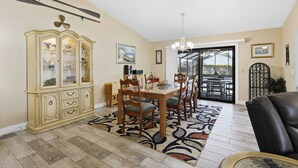 Un coin repas comprenant une table en bois, des chaises, un tapis à motifs, un buffet et un lustre.