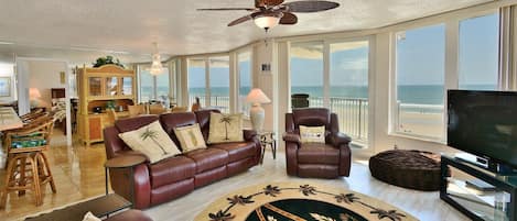 A spacious living room with a leather sofa, a television, and a view of the beach.