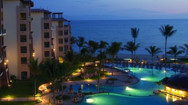 Resort com vários edifícios, área de piscina e palmeiras.