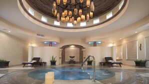 Uma área de spa com uma banheira de hidromassagem circular, cadeiras de descanso e uma fonte central.