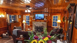A cozy log cabin interior with a fireplace, wooden furniture, and a large window. - Historic Hershey Cabin, Most 10 Star Reviews, Romantic, Just for 2, Immaculate (Lake Arrowhead)
