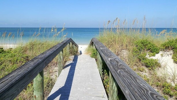 A wooden boardwalk leading to a beach with clear blue water and sandy dunes. - Steps2Beach-Walk everywhere-Bikes & gear Included (St Pete BEach)