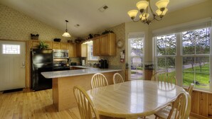 A kitchen with wooden cabinets, a black refrigerator, a wooden dining table with chairs, and a window with a view of the outdoors. - Amy's Waterfront Blessing w/ Hot Tub, Arcade , & Fishing 2 King Master Suites (Pigeon Forge)