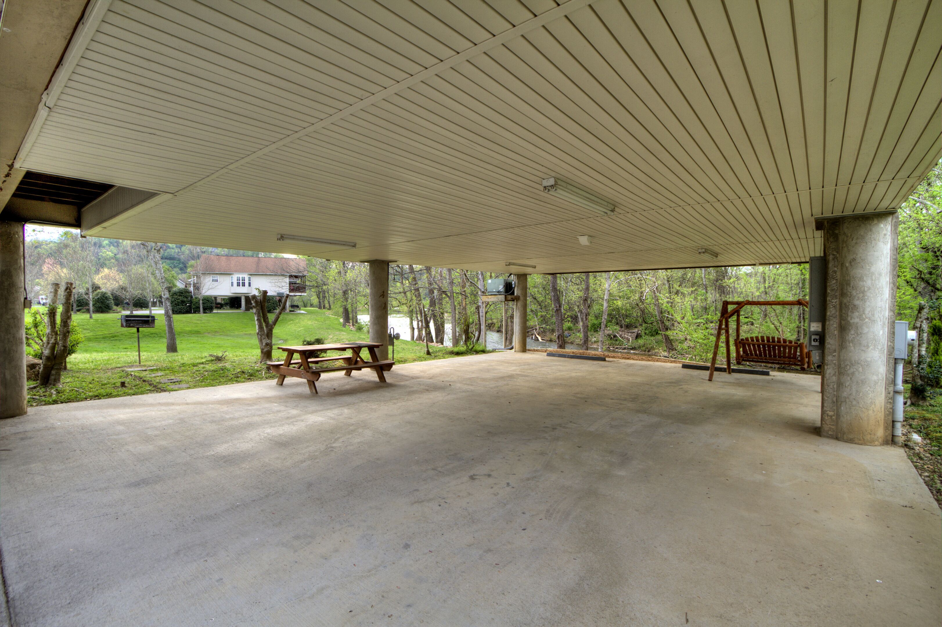 A covered picnic area with a concrete floor, picnic table, benches, and a swing set.