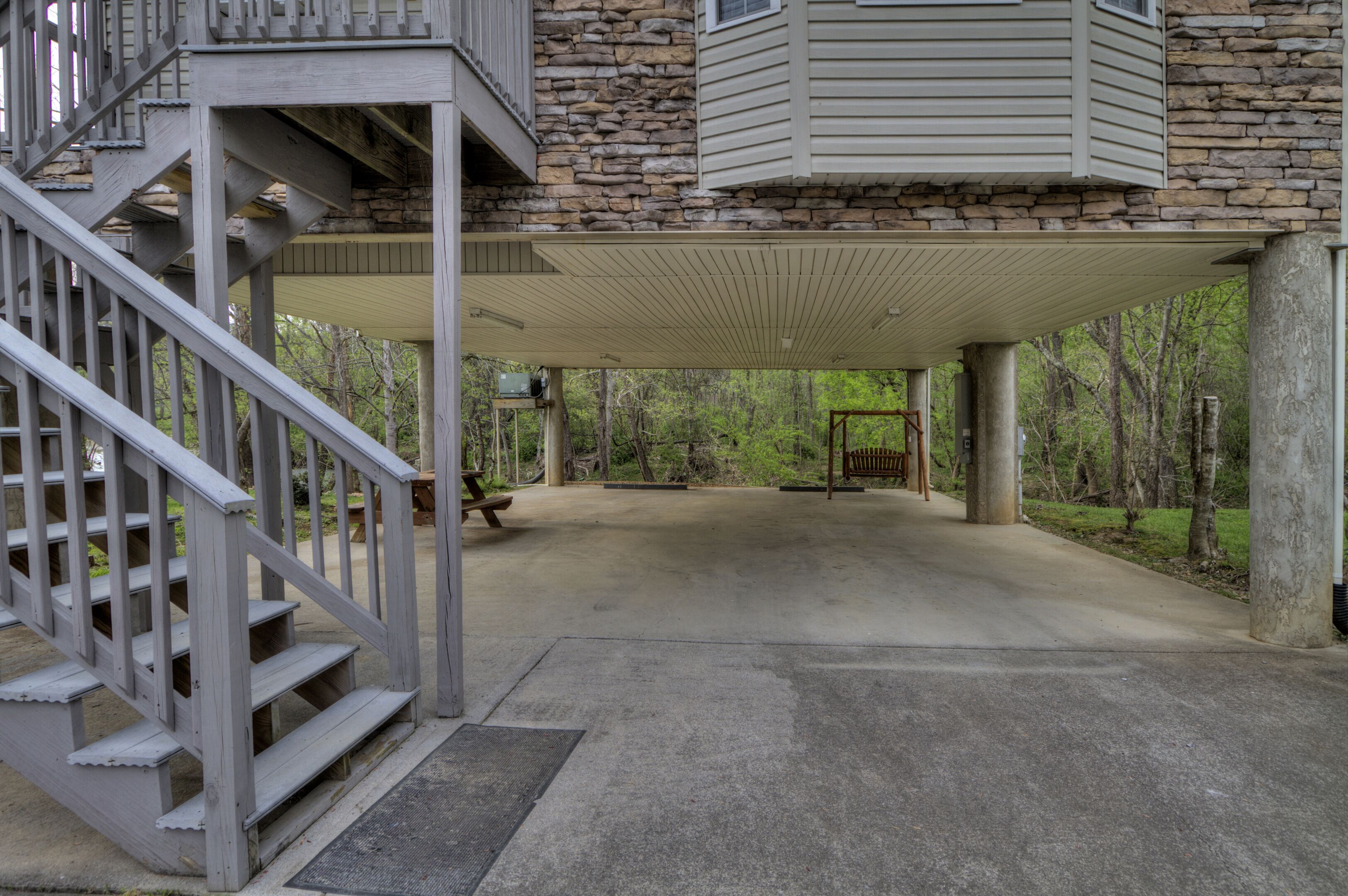 A covered outdoor area with a stone building, a wooden staircase, and a bench.