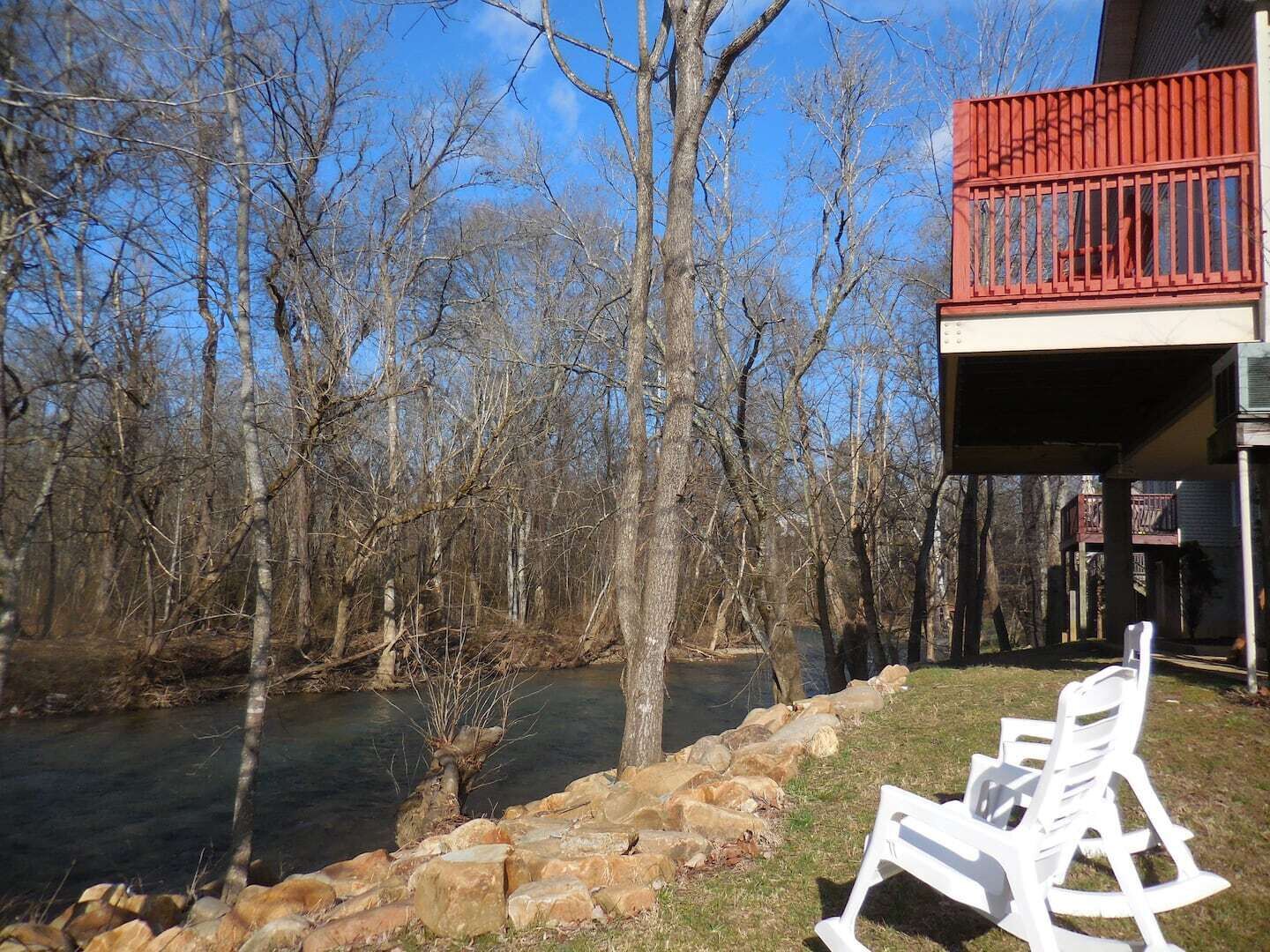 A riverside view with a wooden dock, a white rocking chair, and a building with a red balcony.