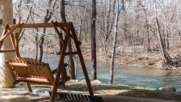 A wooden swing chair by a river with trees in the background. - Amy's Waterfront Blessing w/ Hot Tub, Arcade , & Fishing 2 King Master Suites (Pigeon Forge)