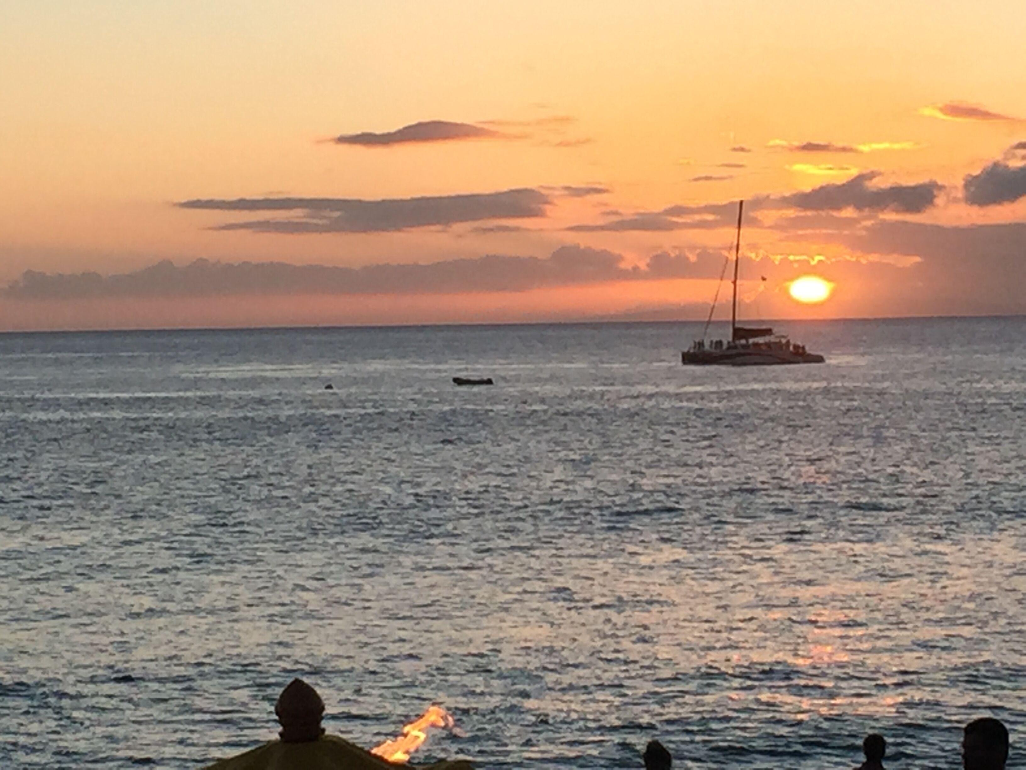 A sunset over a calm sea with a boat and a person holding a torch in the foreground.