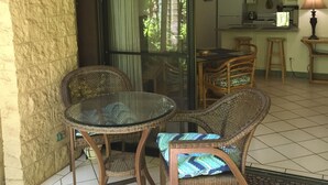 Uma varanda com móveis de vime, uma porta de vidro que dá para uma cozinha e um candeeiro suspenso.
