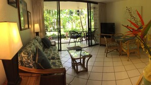 Sala de estar com sofá, cadeiras, mesa de centro, televisão e uma janela grande com vista para o verde.