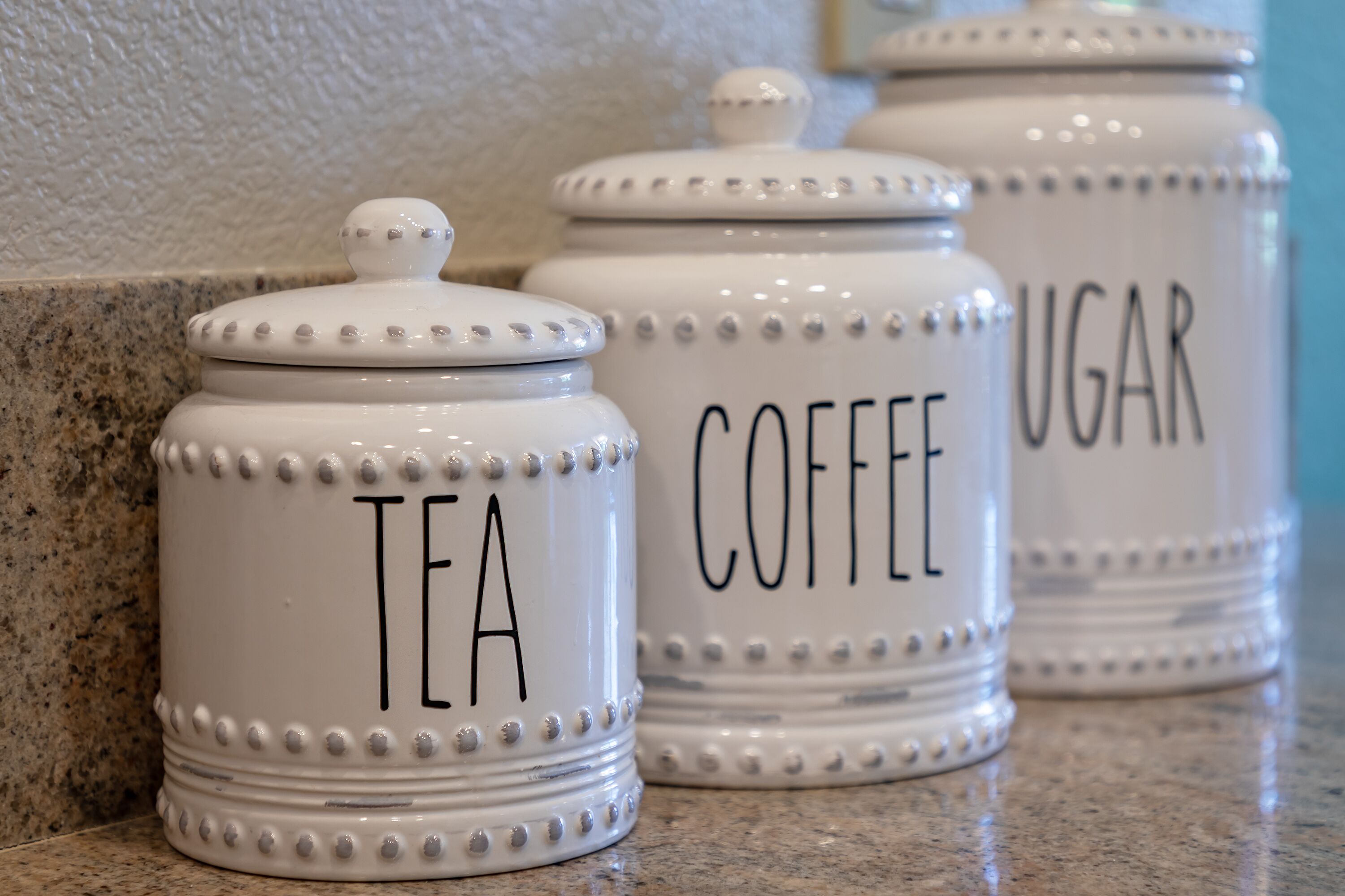 Three white ceramic containers with labels for tea, coffee, and sugar.