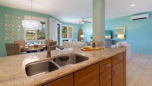A kitchen with granite countertops, stainless steel sink, wooden cabinets, and a ceiling fan. - 5 Star Ocean View, Beach House Chic, Click the Video tour below! (Wailea)