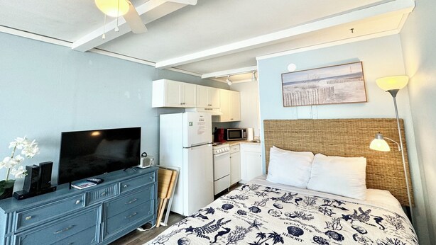 Une chambre d’hôtel équipée d’un lit, d’une télévision, d’un ventilateur de plafond, d’un four à micro-ondes et d’une kitchenette.