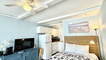 A hotel room with a bed, a TV, a ceiling fan, a microwave, and a kitchenette.