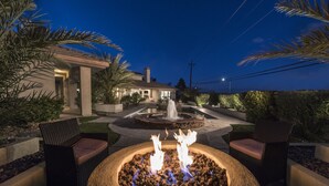 A patio area with a fire pit, outdoor seating, and a fountain.