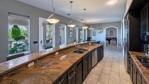 A modern kitchen with a long island, stainless steel appliances, and pendant lighting.