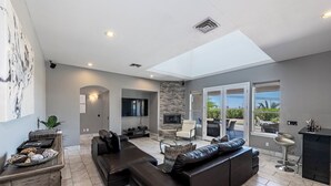 A spacious living room with a large sectional sofa, a flat-screen TV, a fireplace, and a balcony with outdoor seating.