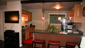 A compact kitchen with a built-in TV, wooden cabinets, a refrigerator, and a coffee maker. - The 8th Street Retreat Looks Booked it may not be Call Us (Carbondale)