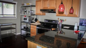 A modern kitchen with granite countertops, wooden cabinets, stainless steel appliances, and a window with blinds. - The 8th Street Retreat Looks Booked it may not be Call Us (Carbondale)