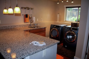 A kitchen with granite countertops, a built-in sink, a washing machine, and a window with blinds.