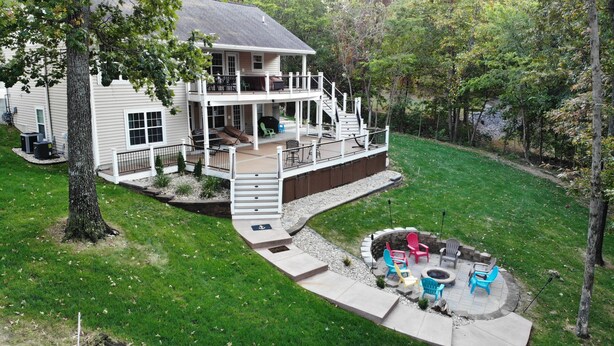 Ein zweigeschossiges Haus mit überdachter Terrasse, Feuerstelle und Gartenmöbeln.