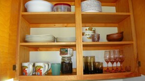 Un mueble de madera con estantes que contienen diverso menaje de cocina y cristalería.