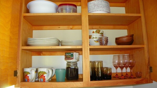 A wooden cabinet with shelves containing various kitchenware and glassware.